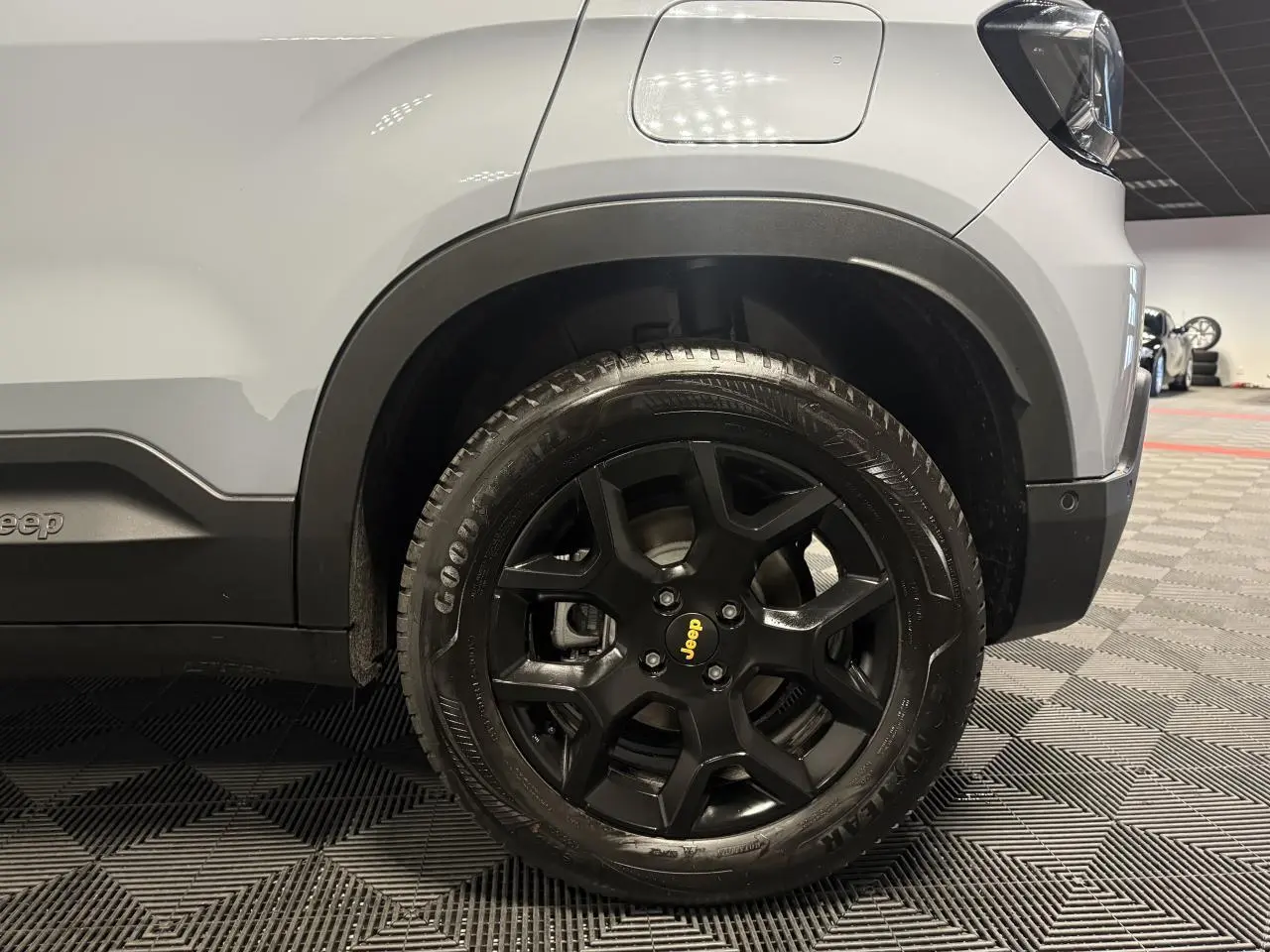 Gros plan sur la roue avant droite noire avec logo Jeep jaune, sur carrosserie gris clair du Jeep Avenger.