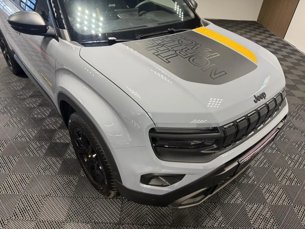 Vue 3/4 avant gauche du Jeep Avenger gris avec capot noir mat marqué The North Face et jantes noires.