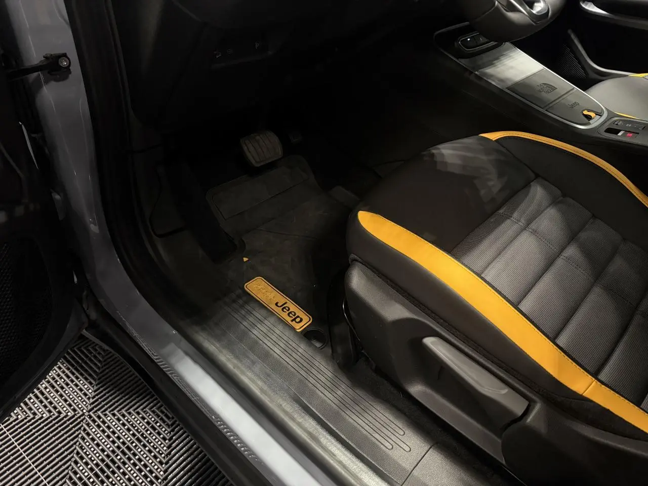 Vue intérieure côté conducteur du Jeep Avenger gris, avec siège noir et jaune et tapis de sol marqué Jeep.