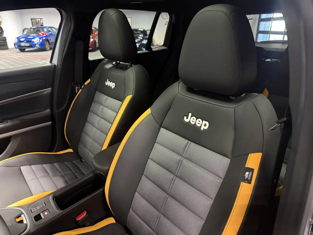 Vue intérieure sur les sièges avant gris et noir avec surpiqûres jaunes et logo Jeep brodé sur appuie-têtes.
