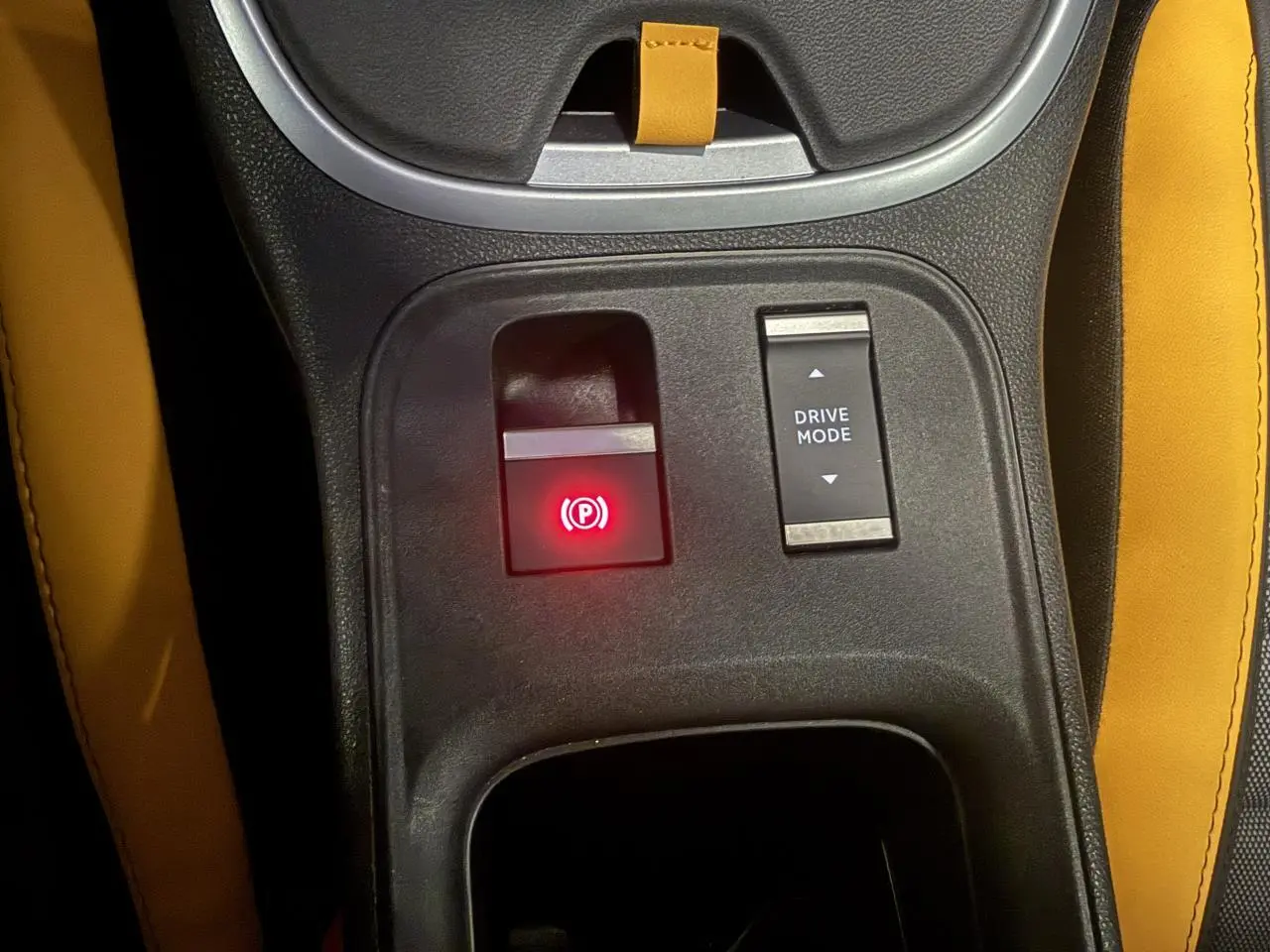Vue rapprochée du frein de stationnement électrique et bouton Drive Mode sur la console centrale avec sellerie jaune du Jeep Avenger Hybrid 4xe.
