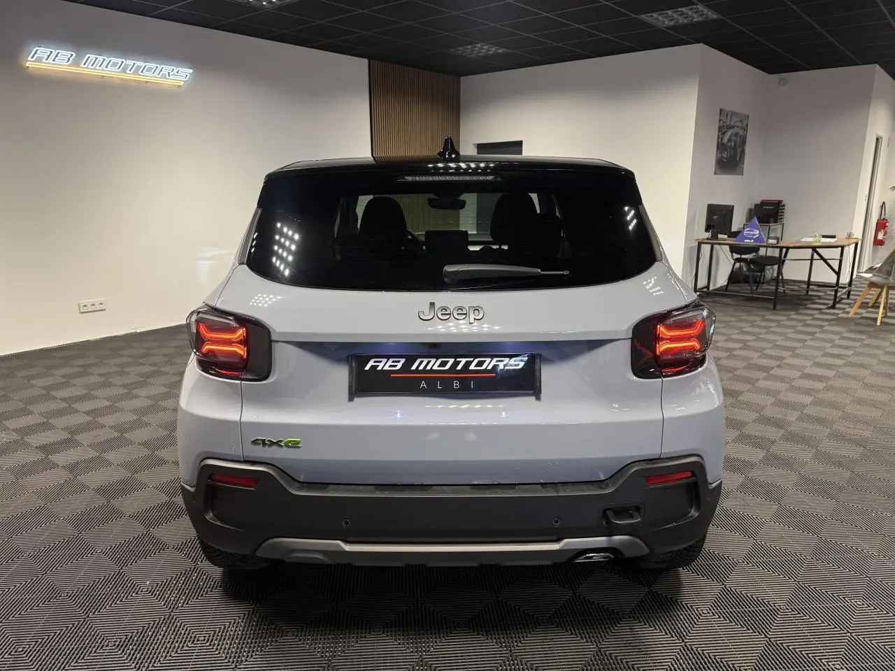 Vue arrière d'un Jeep Avenger gris avec toit noir et feux arrière LED allumés dans un showroom.
