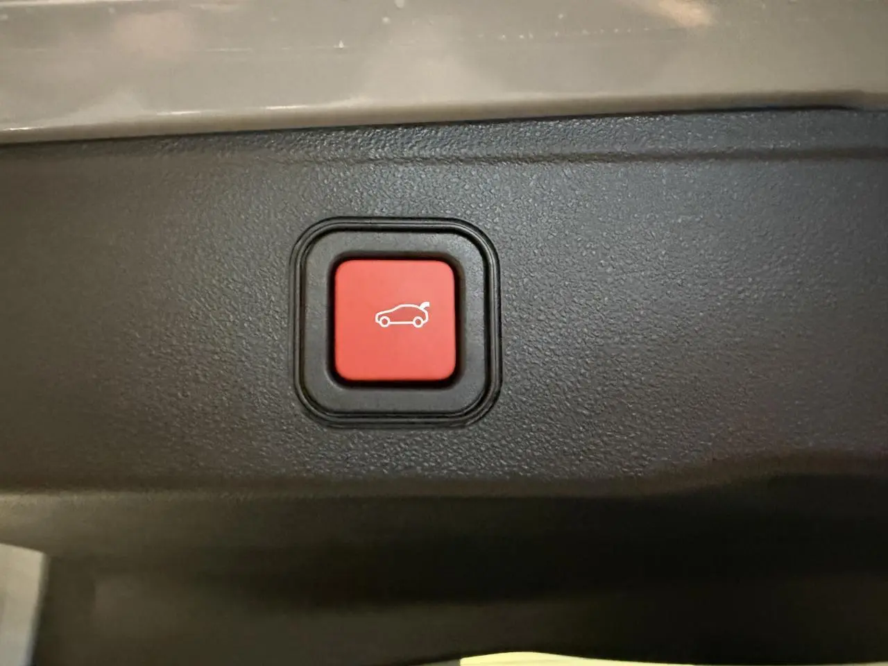 Gros plan sur bouton rouge d'ouverture électrique du coffre dans l'habitacle du Jeep Avenger gris.