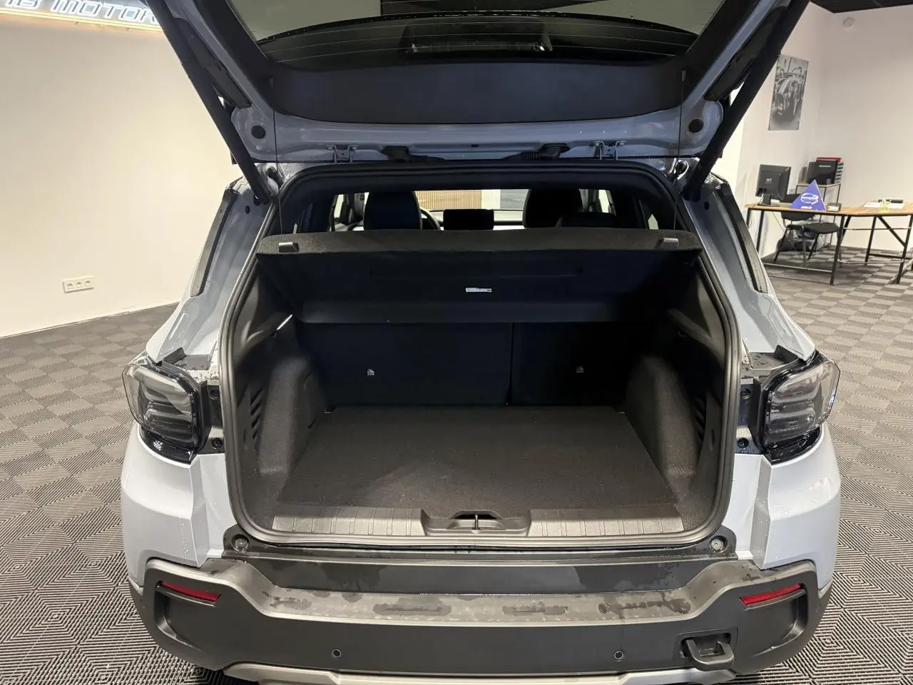 Vue arrière du coffre ouvert d'un Jeep Avenger gris avec toit ouvrant en verre dans un showroom.