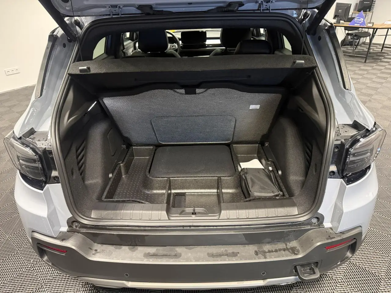 Coffre ouvert vu de l'arrière d'un Jeep Avenger gris avec intérieur de coffre compartimenté et banquette arrière visible.