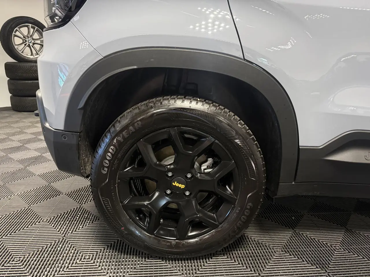 Gros plan sur la roue avant gauche noire avec jante alliage Jeep sur carrosserie gris clair du Jeep Avenger Hybrid 4xe.
