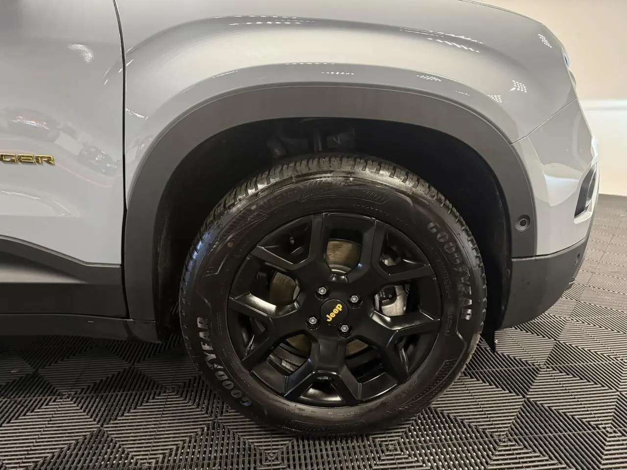 Gros plan sur la roue avant droite noire mat d’un Jeep Avenger gris avec badge jaune et jante 17 pouces.
