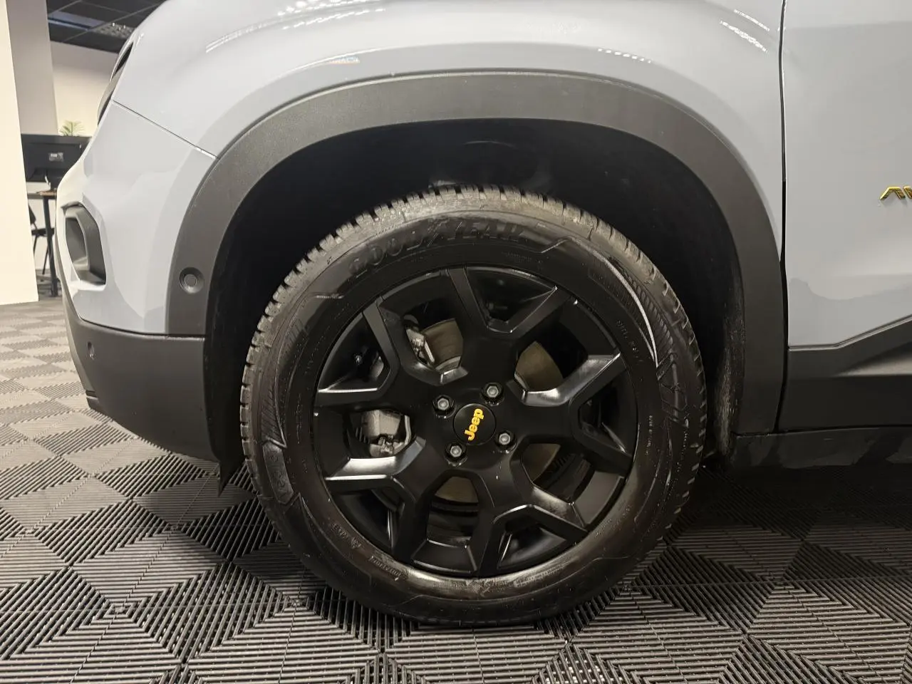 Gros plan sur la roue avant gauche noire avec jante alliage noir mat et partie de la carrosserie gris clair du Jeep Avenger.