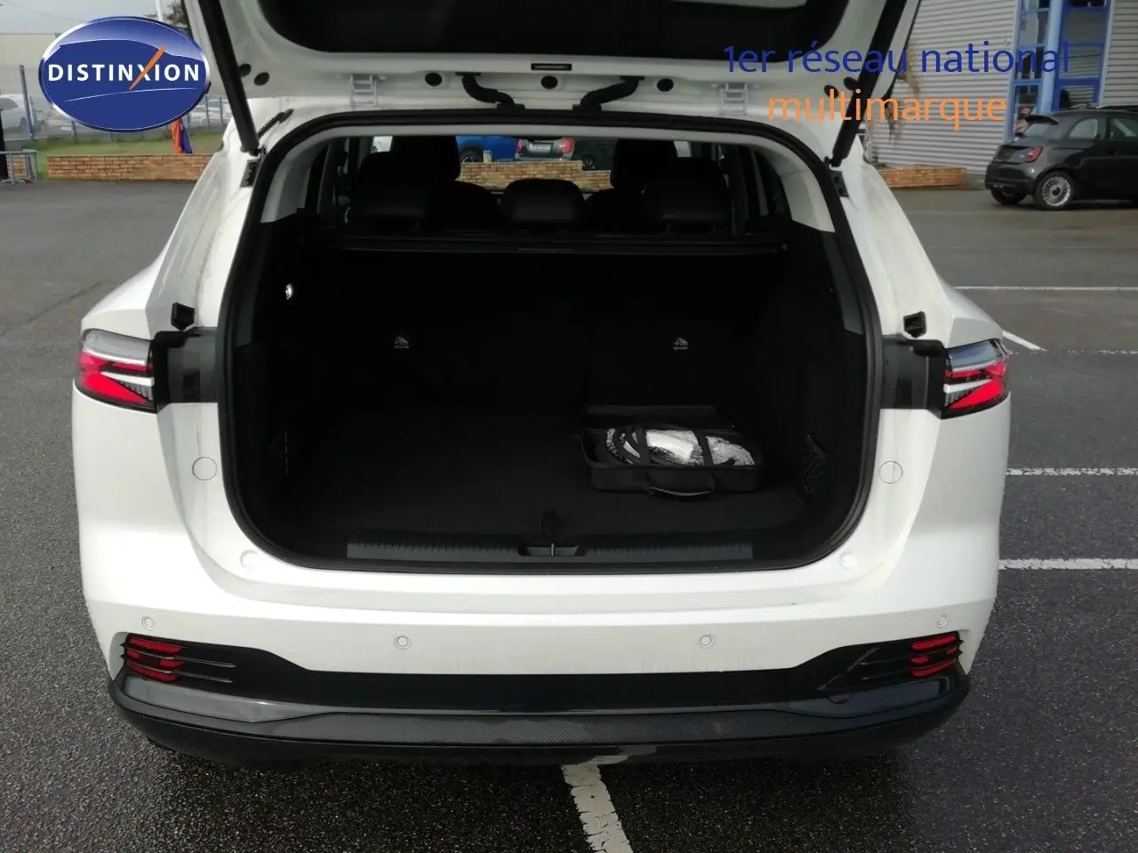 Vue arrière d'un MG MOTOR EHS 1.5T PHEV 272CH Luxury blanc nacré avec coffre ouvert et intérieur noir visible.