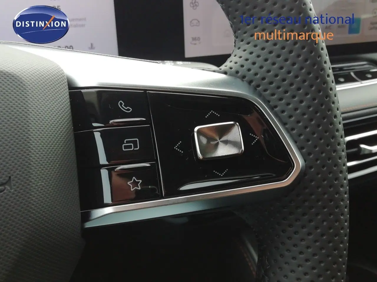 Gros plan sur les commandes gauche du volant perforé noir du MG MOTOR EHS blanc perle, avec écran tactile en arrière-plan.