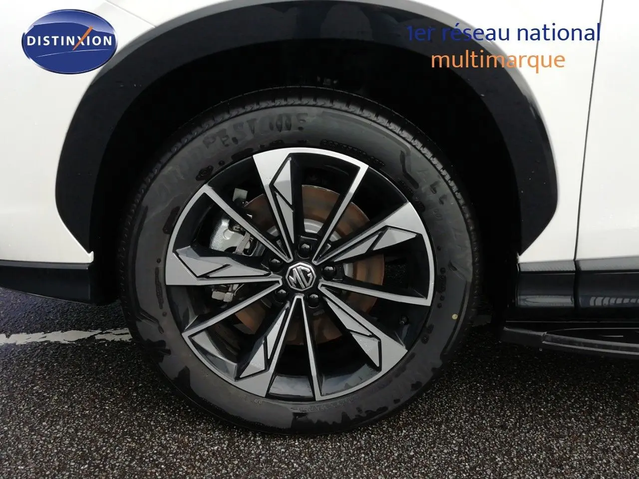 Gros plan sur la roue avant droite d’un MG MOTOR EHS 1.5T PHEV 272CH Luxury blanc nacré avec jante alliage bicolore.