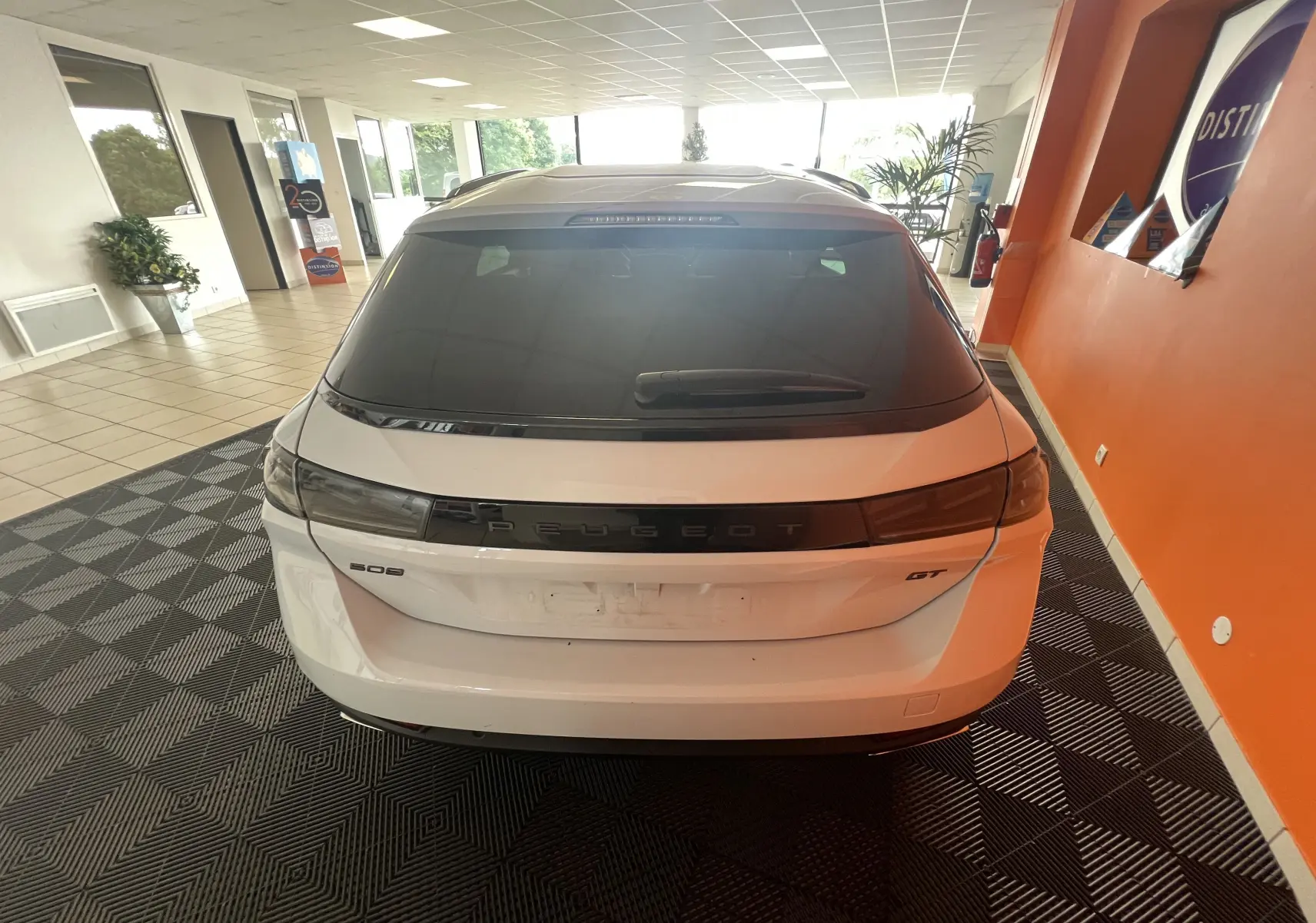 Vue arrière d'un Peugeot 508 SW GT blanc stationné en intérieur avec vitres arrière surteintées et logo Peugeot noir.