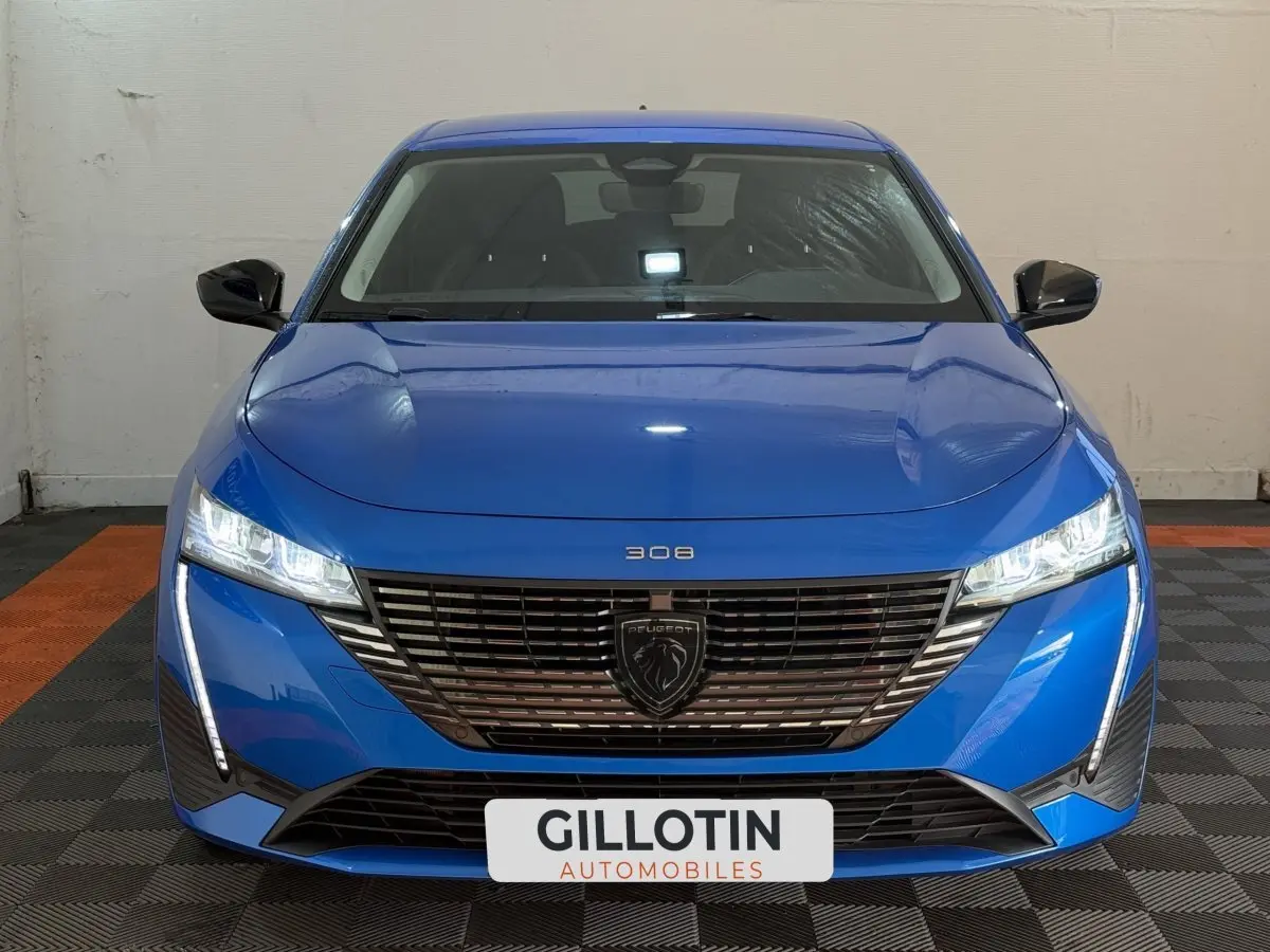 Vue frontale d'une Peugeot 308 bleu vif avec calandre noire et phares LED allumés dans un garage.