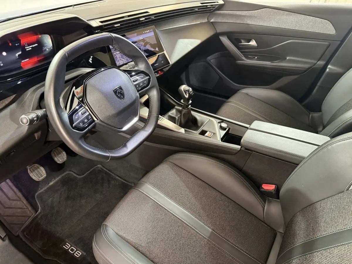 Intérieur noir de la Peugeot 308 2023, vue côté conducteur, volant cuir, écran tactile et boîte manuelle visibles.