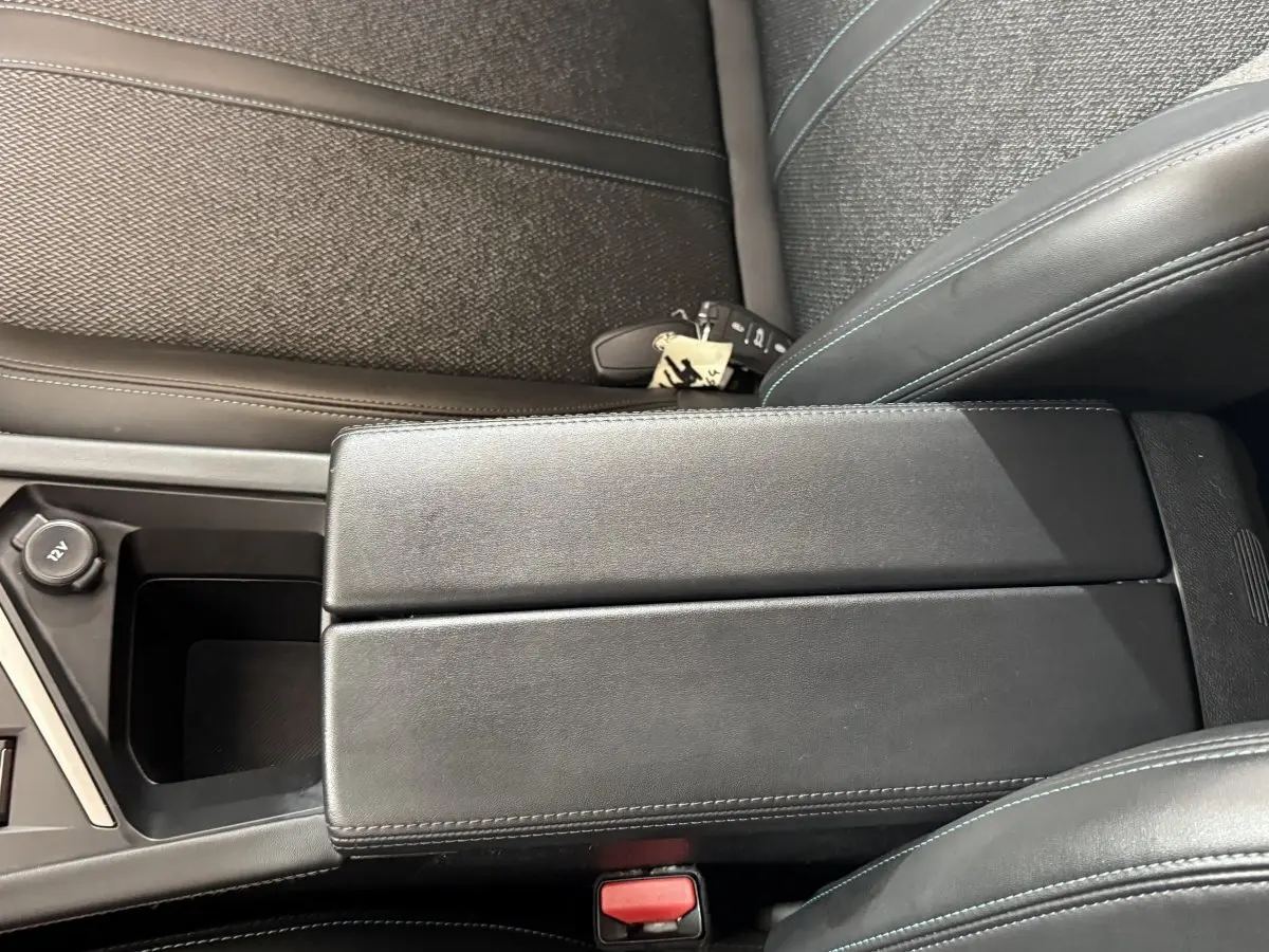 Vue rapprochée de l'accoudoir central noir et des sièges en tissu bleu foncé de la Peugeot 308 2023.