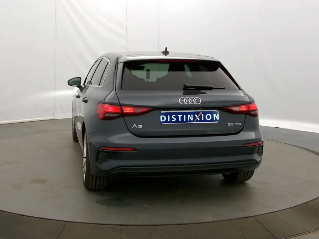 Vue arrière d'une Audi A3 Sportback 35 TDI gris Manhattan de 2021 avec feux arrière allumés dans un studio.