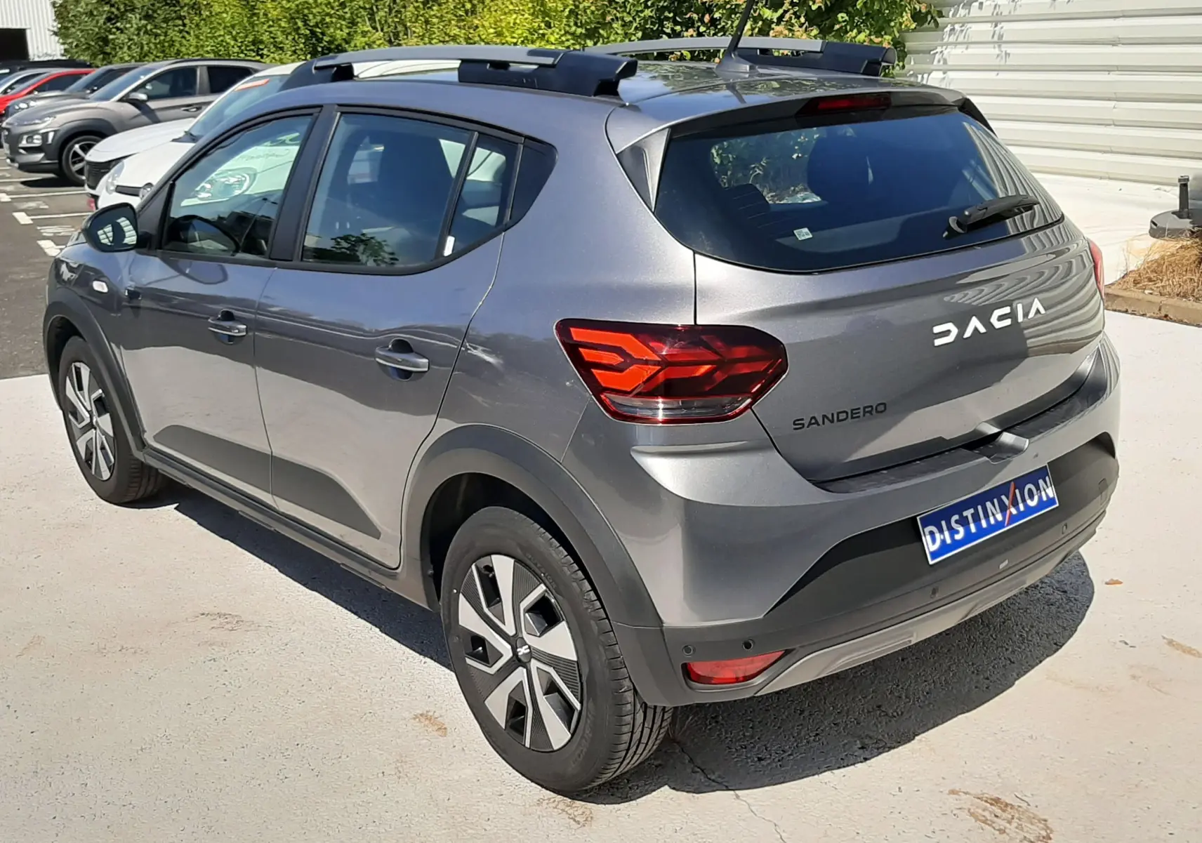 Vue 3/4 arrière droite d'une Dacia Sandero Stepway gris schiste avec barres de toit et feux arrière LED.
