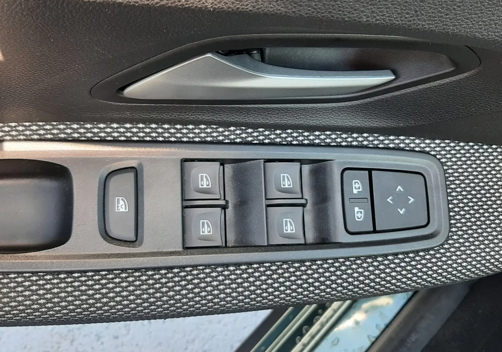 Détail des commandes des vitres et rétroviseurs sur la porte côté conducteur d'une Dacia Sandero Stepway gris schiste.