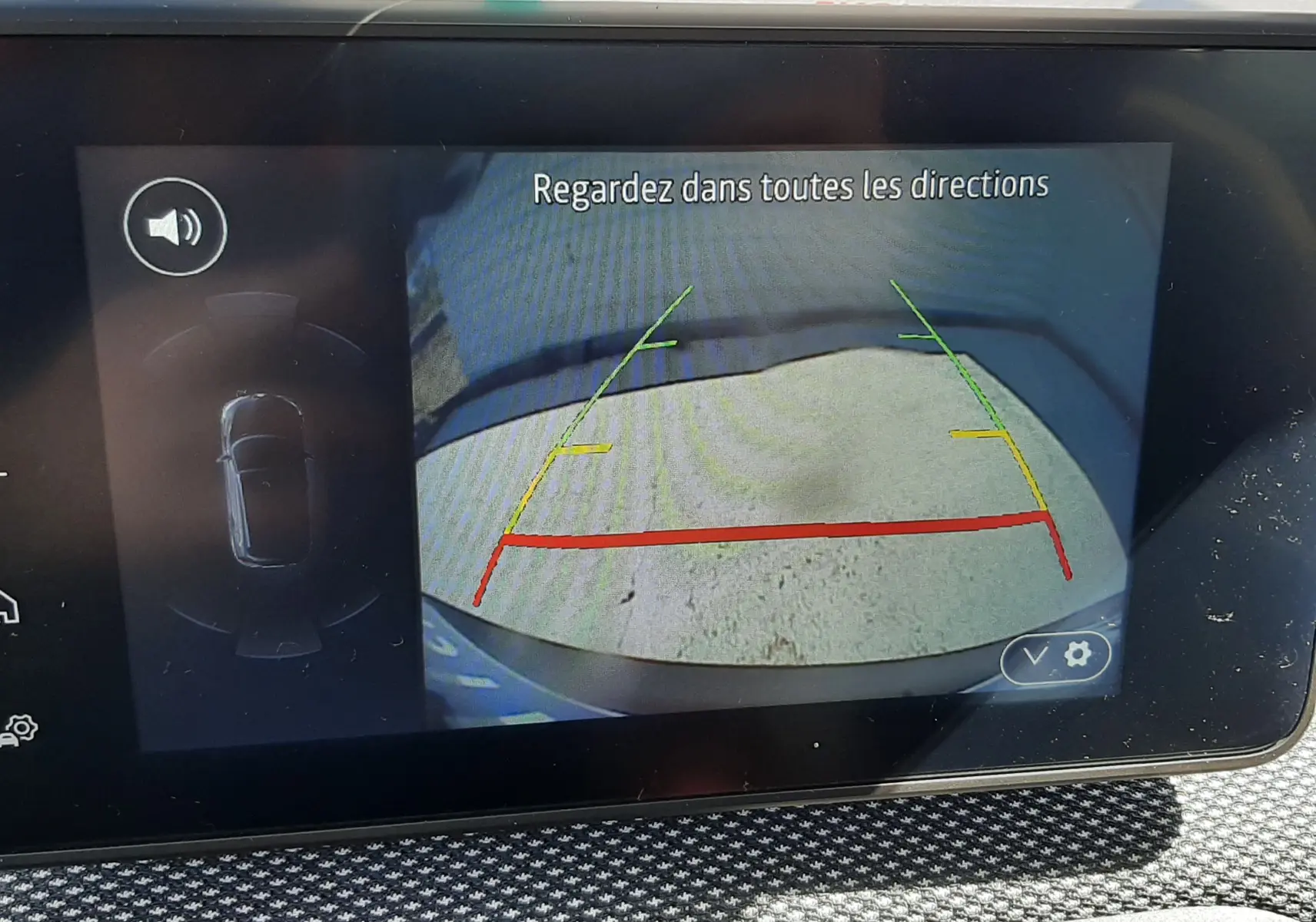 Écran multimédia montrant la caméra de recul d'une Dacia Sandero Stepway gris schiste, avec lignes de guidage colorées.