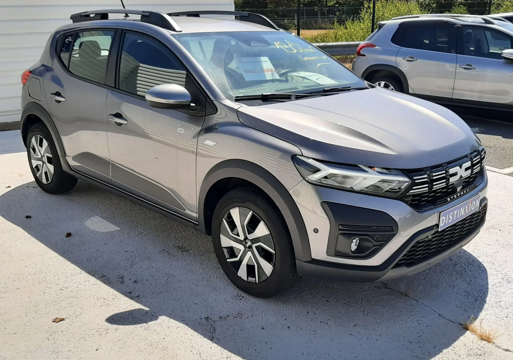 Vue 3/4 avant droite d'une Dacia Sandero Stepway gris schiste avec barres de toit et jantes alliage distinctives.