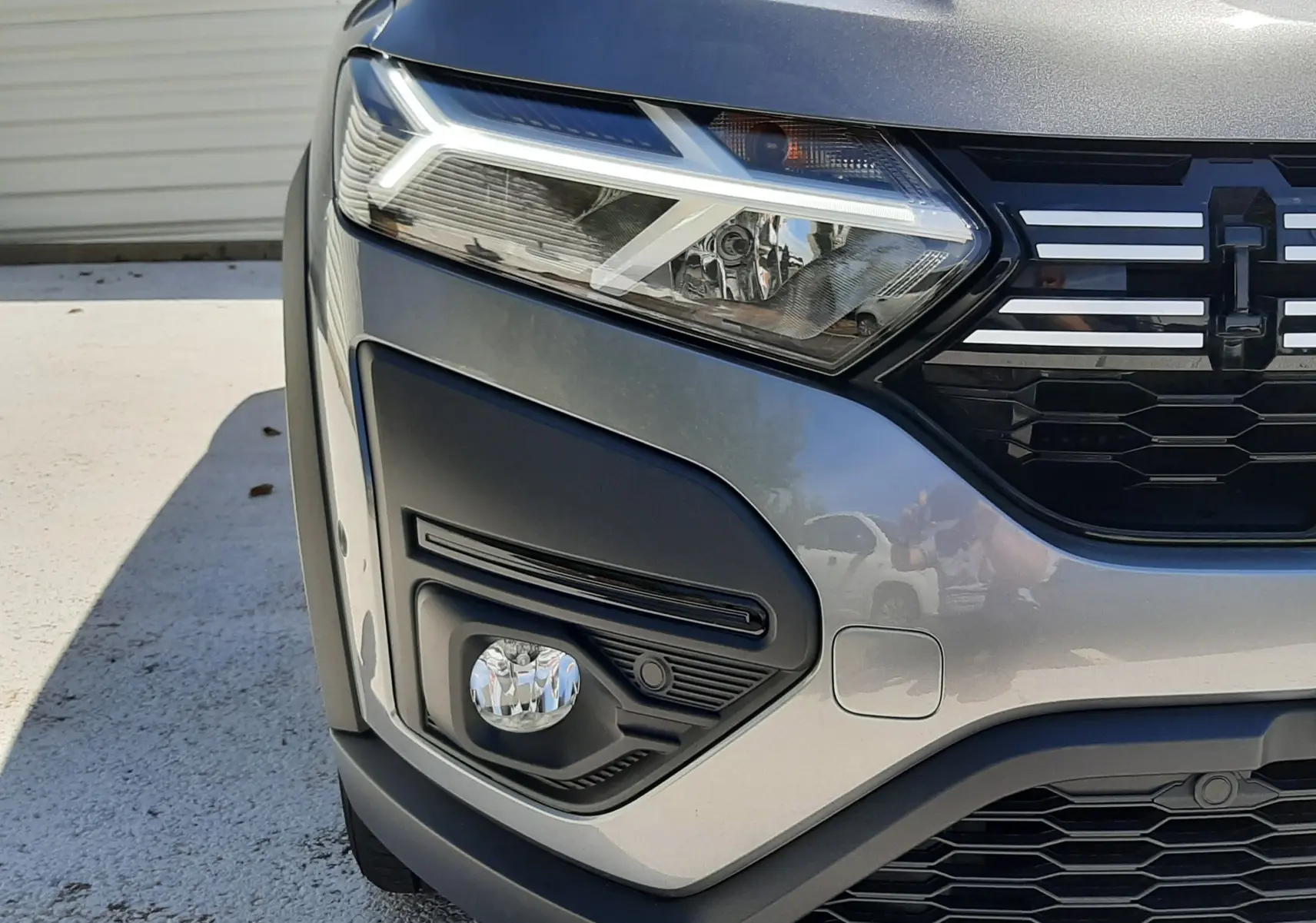 Gros plan sur l'avant gauche de la Dacia Sandero Stepway gris schiste, mettant en valeur le phare LED et la calandre noire.