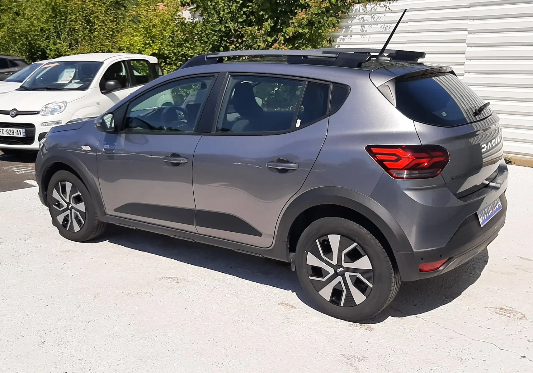 Dacia Sandero Stepway gris schiste vue 3/4 arrière droit, avec barres de toit et jantes spécifiques.
