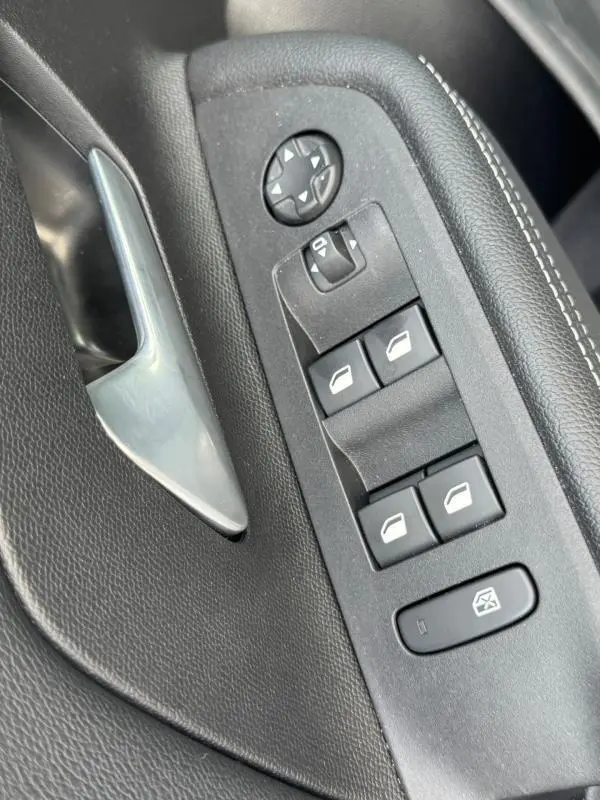 Gros plan sur la commande des vitres et rétroviseurs côté gauche de la porte intérieure grise de l’Opel Mokka électrique 2025.