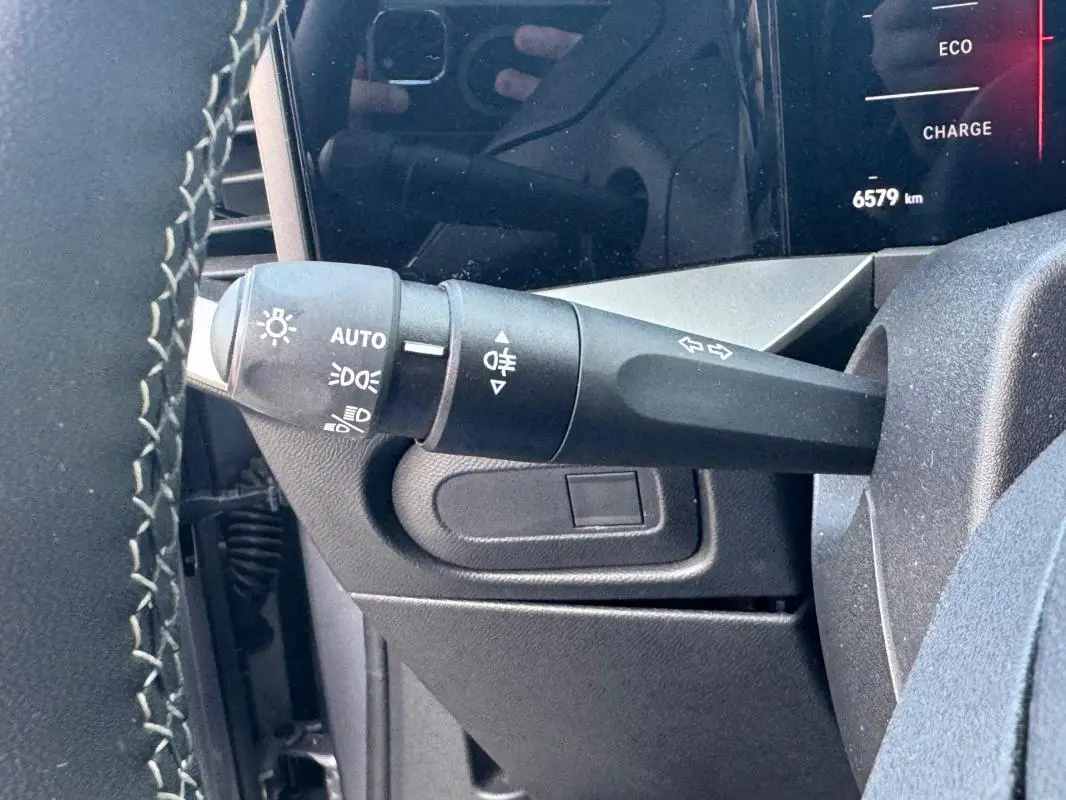Gros plan sur le commodo gauche du volant d’un Opel Mokka électrique gris, affichage digital partiel en arrière-plan.