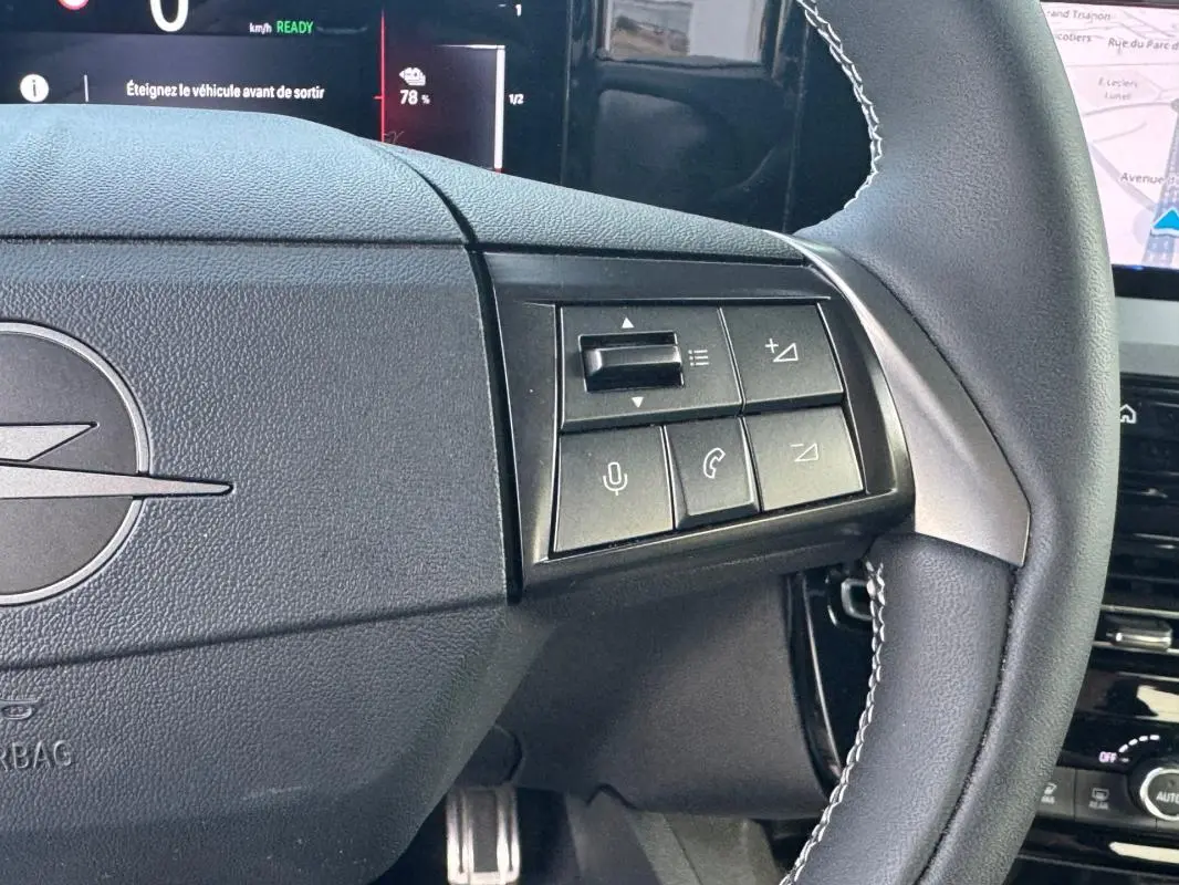 Gros plan sur le volant noir de l’Opel Mokka électrique 2025 avec commandes intégrées et logo Opel visible.