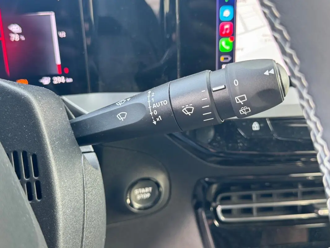 Gros plan sur la commande des essuie-glaces à gauche du volant dans l’habitacle noir de l’Opel Mokka électrique gris 2025.