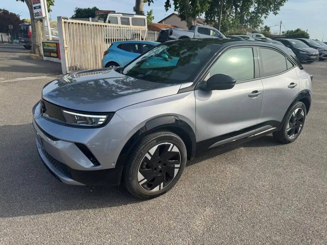 Opel Mokka électrique gris en 3/4 avant droit, avec jantes alliage noires et vitres surteintées.