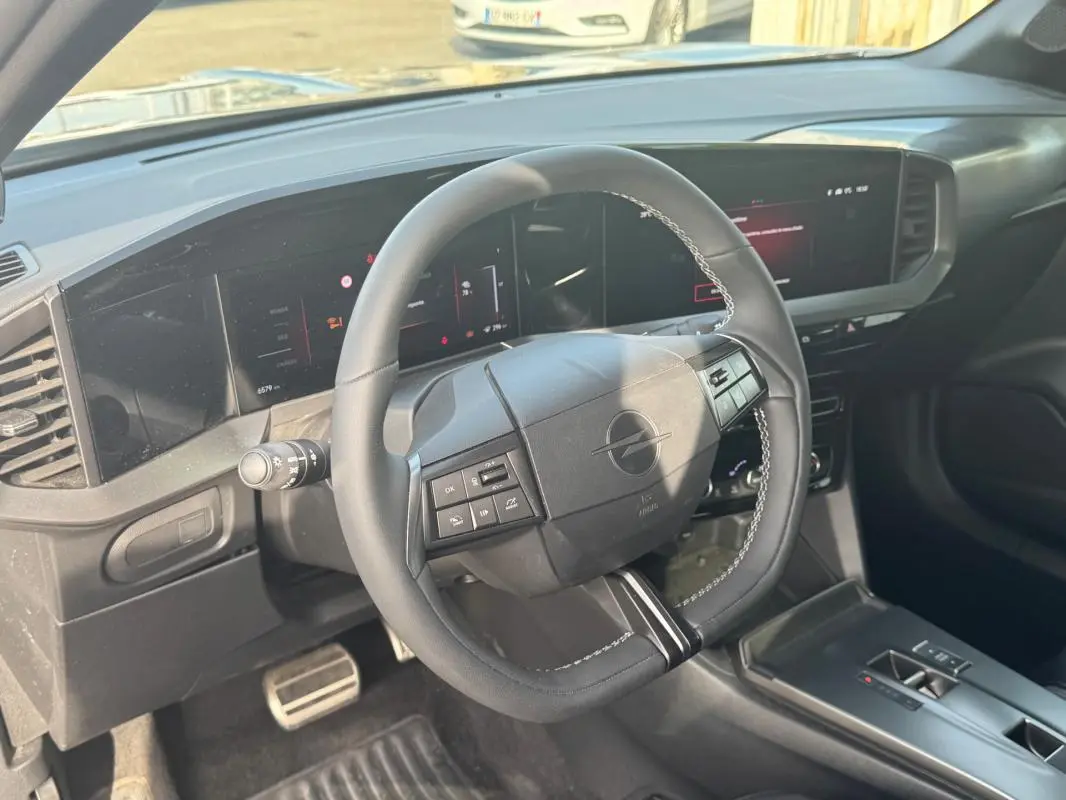 Vue intérieure centrée sur le volant noir avec coutures blanches de l'Opel Mokka électrique 2025, tableau de bord digital.