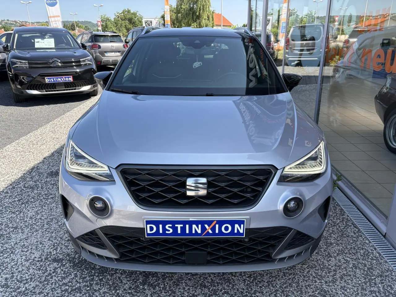 Vue avant d'une SEAT Arona 2024 gris clair, avec calandre noire et phares LED anguleux, sur parking extérieur.