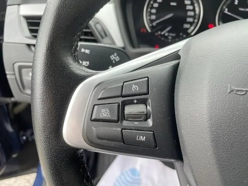 Gros plan sur les commandes de régulateur de vitesse au volant d'une BMW X2 bleu métal 2021, version Lounge.