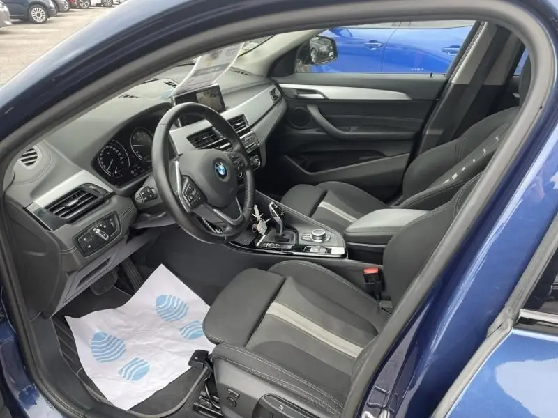 Vue intérieure côté conducteur de la BMW X2 bleu métal 2021, montrant le tableau de bord et les sièges sport noirs.