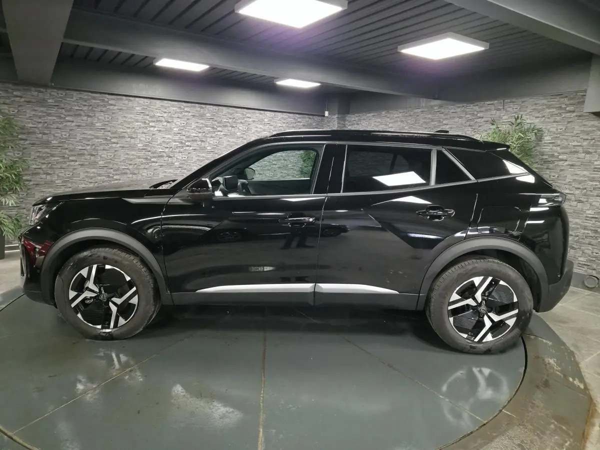 Profil côté gauche du Peugeot 2008 noir brillant avec jantes alliage bi-ton dans un showroom intérieur.