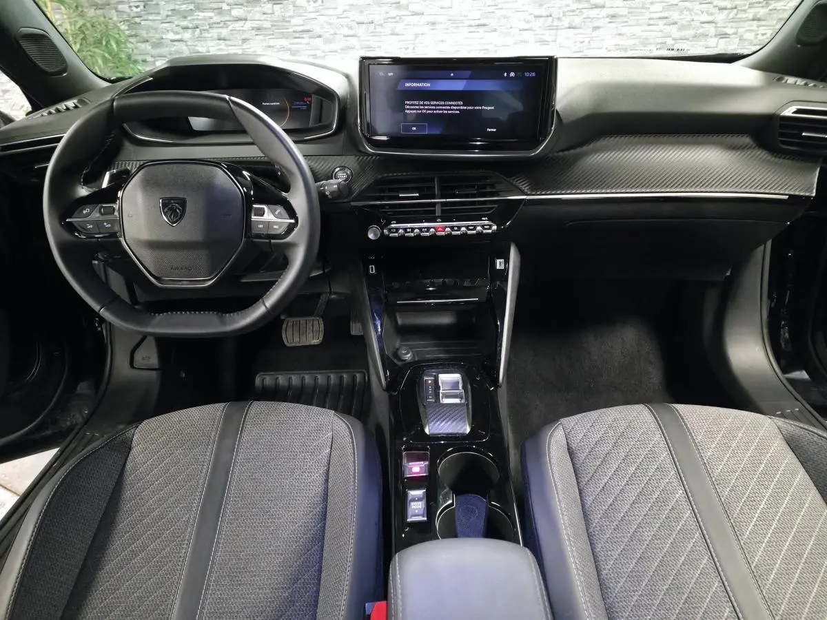 Vue intérieure avant du Peugeot 2008 2025 noir, avec tableau de bord carbone et écran tactile central.