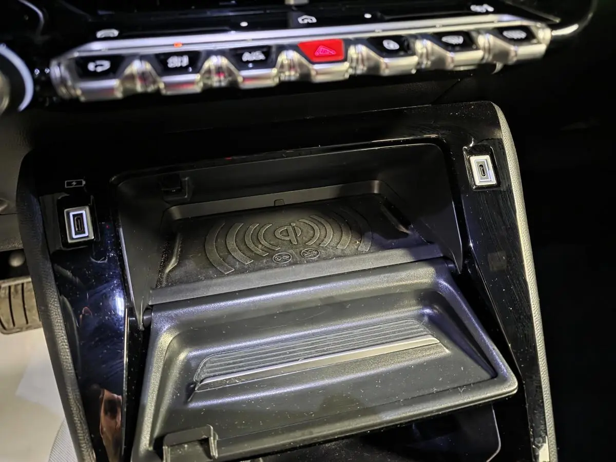Gros plan sur la console centrale noire du Peugeot 2008 2025 avec zone de recharge sans fil et ports USB.