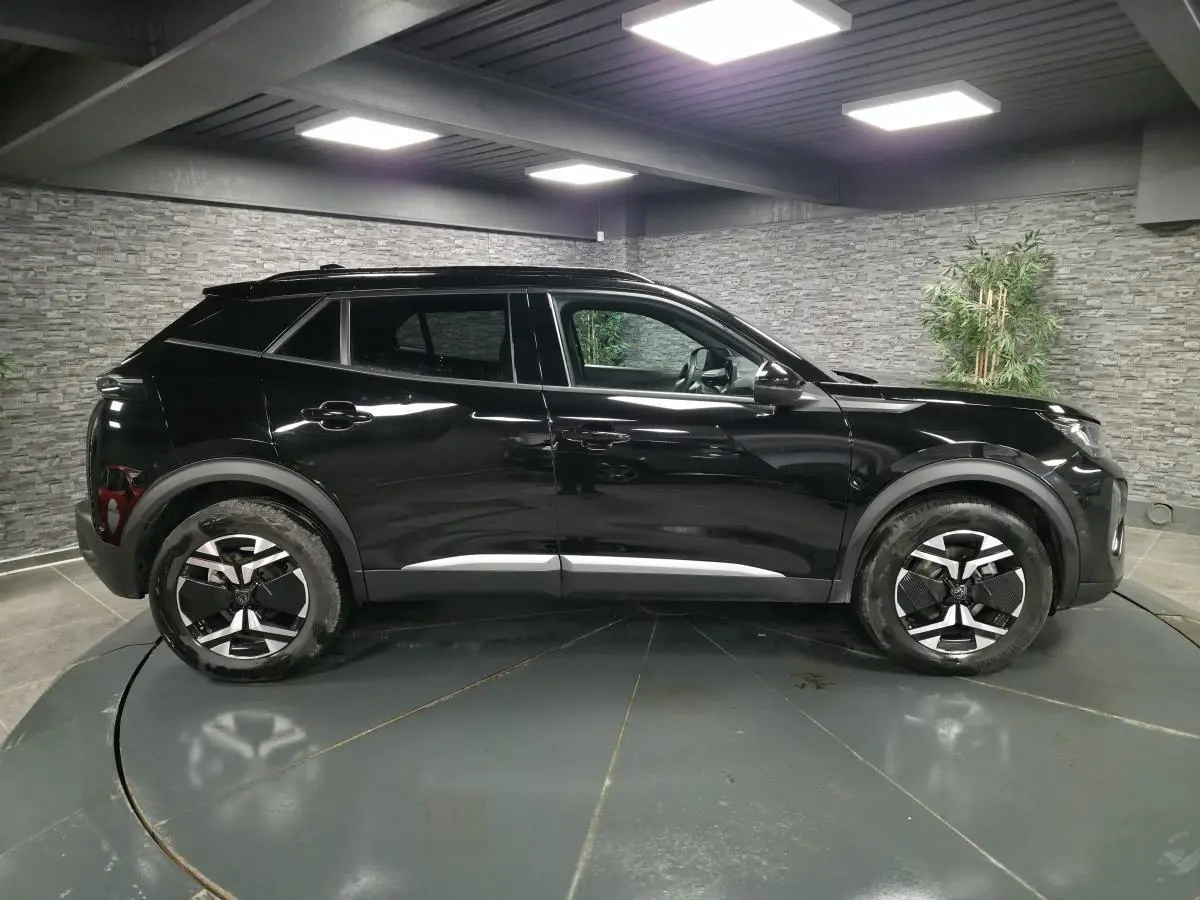 Vue latérale droite d’un Peugeot 2008 noir brillant avec jantes alliage bi-ton et barres de toit noires.