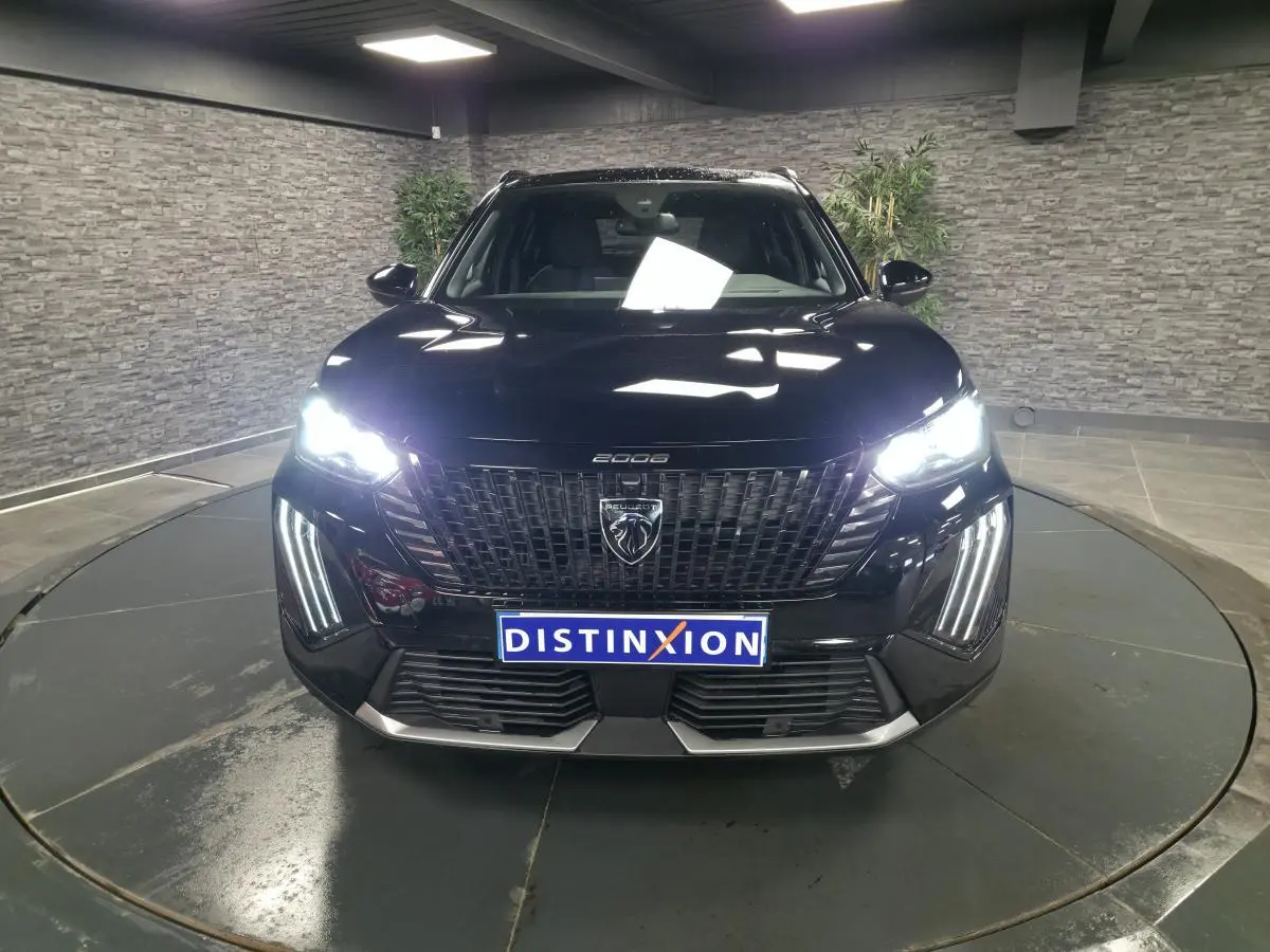 Vue frontale d'un Peugeot 2008 noir avec feux allumés et calandre noire à l'intérieur moderne.