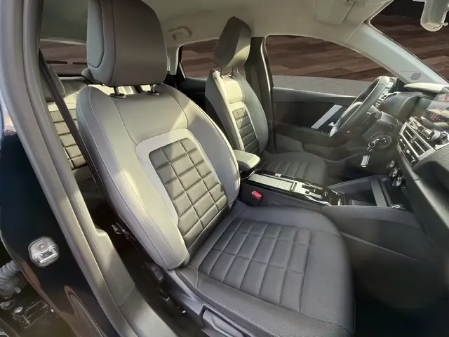 Vue intérieure côté conducteur de la Citroën C4 Hybride 145 e-DSC6 PLUS 2025, sièges tissu gris et tableau de bord moderne.
