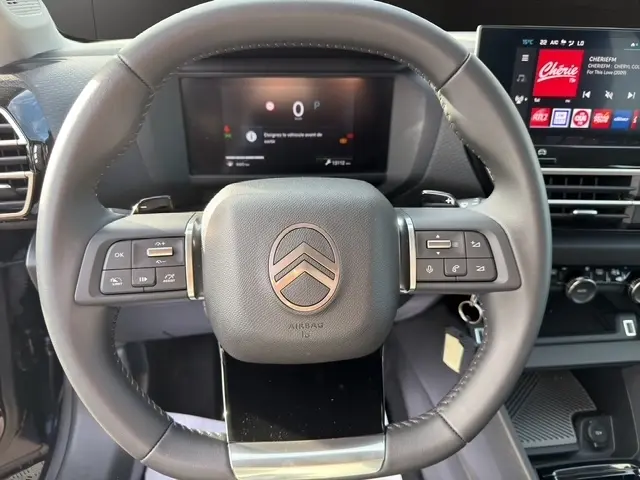 Vue rapprochée du volant cuir multifonctions de la Citroën C4 hybride 2025 avec tableau de bord numérique et écran tactile.