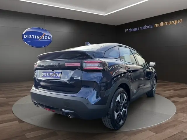 Vue 3/4 arrière droite d'une Citroën C4 hybride bleu foncé avec feux LED et jantes distinctives en showroom.