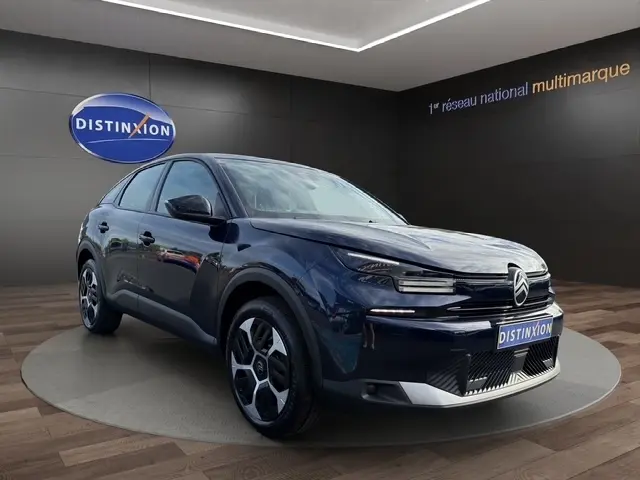 Citroën C4 hybride bleu en 3/4 avant droit, avec phares LED et jantes au design moderne, sur podium intérieur.