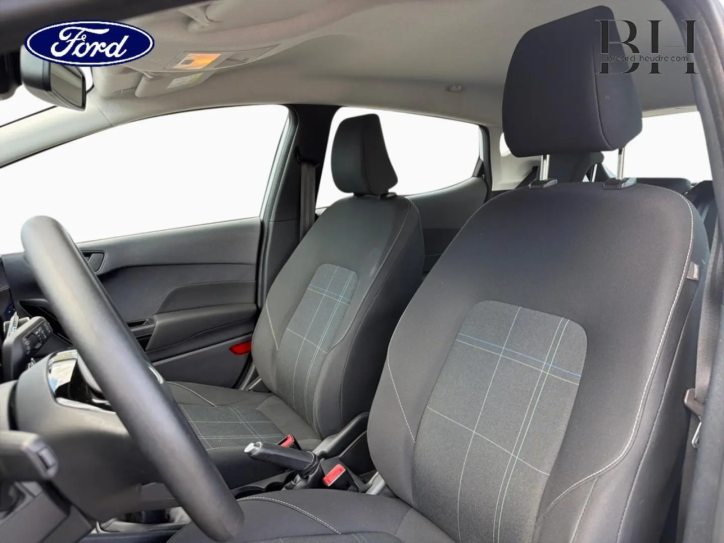 Vue intérieure avant de la Ford Fiesta 2020, sièges tissu noir à motifs, volant et portières visibles, ambiance claire.