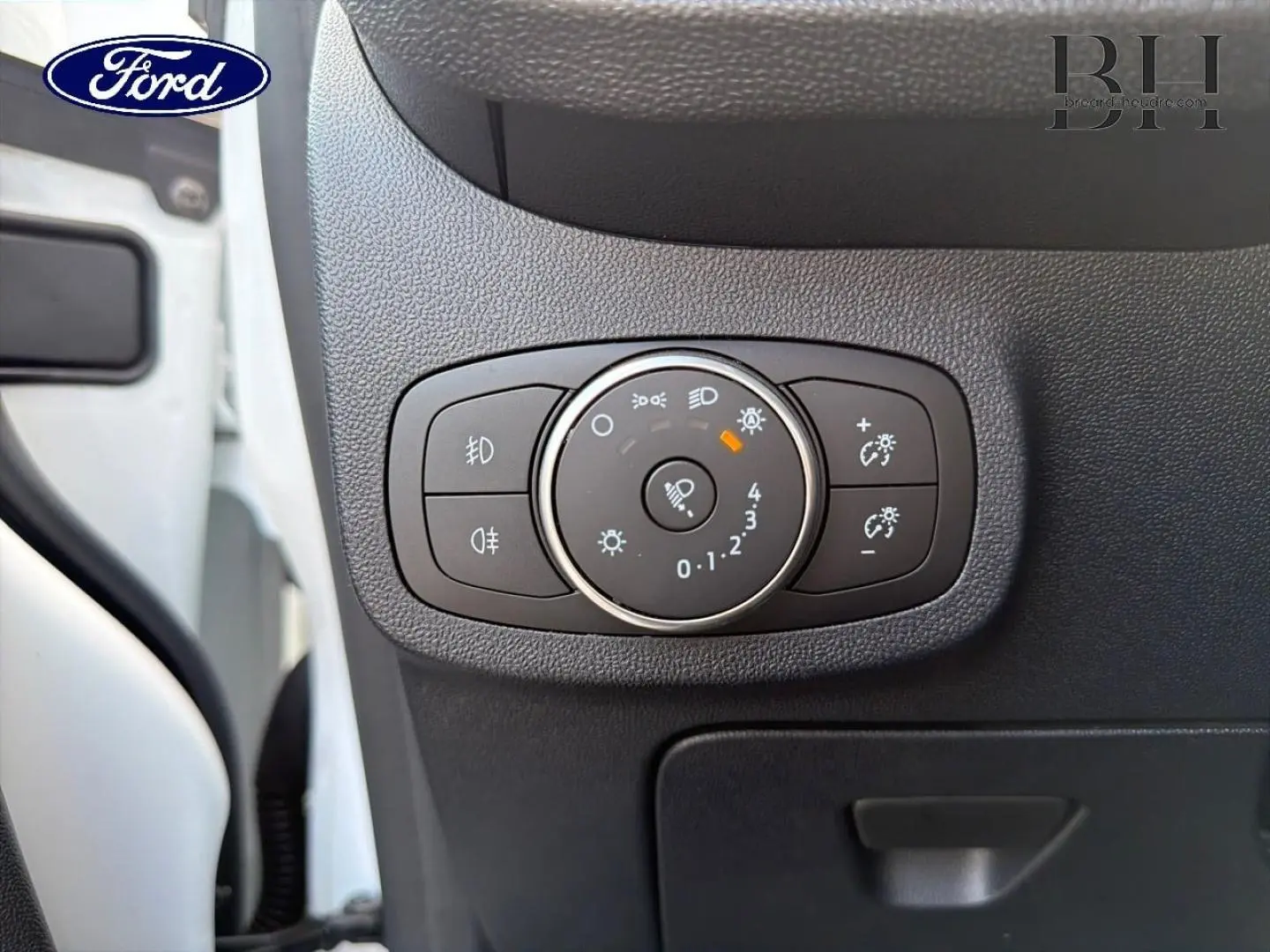 Gros plan sur le bouton de réglage des phares dans l’habitacle d’une Ford Fiesta blanche, côté conducteur.
