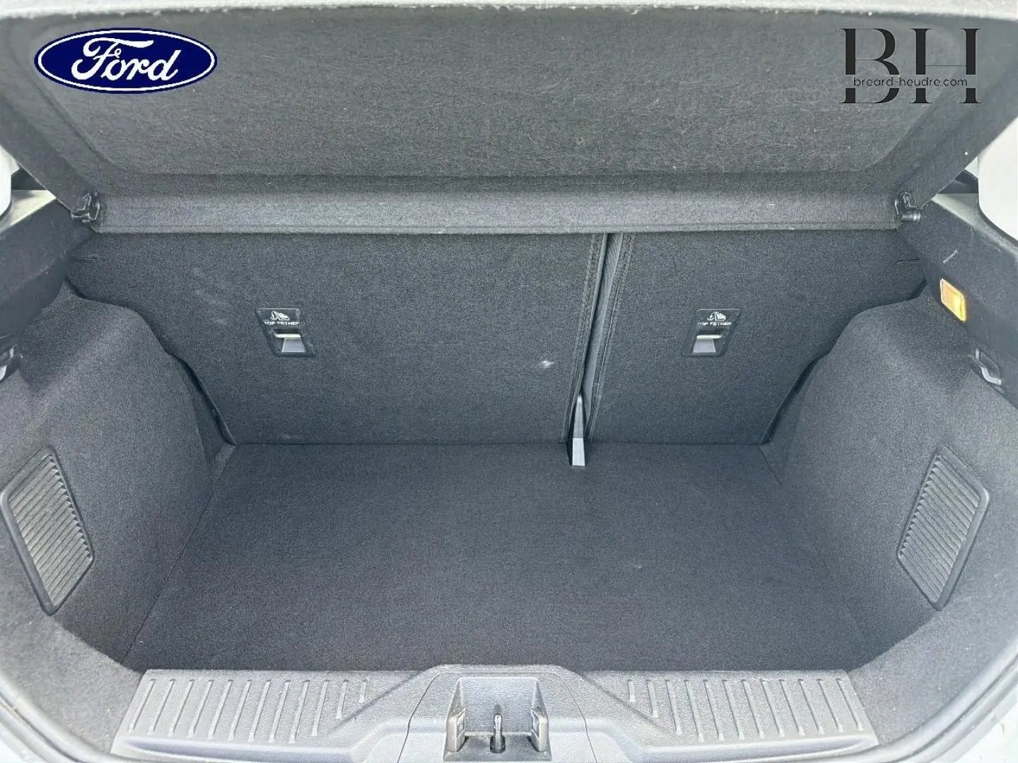 Coffre ouvert d'une Ford Fiesta blanc glacier, vue de l'intérieur montrant l'espace de chargement et la banquette arrière rabattable.