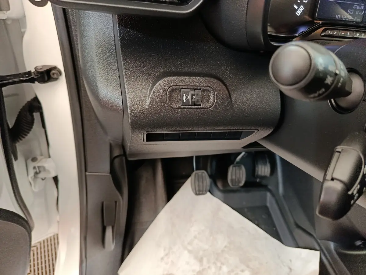 Vue intérieure côté conducteur du Citroën Berlingo blanc 2022, montrant les pédales et commandes du tableau de bord.