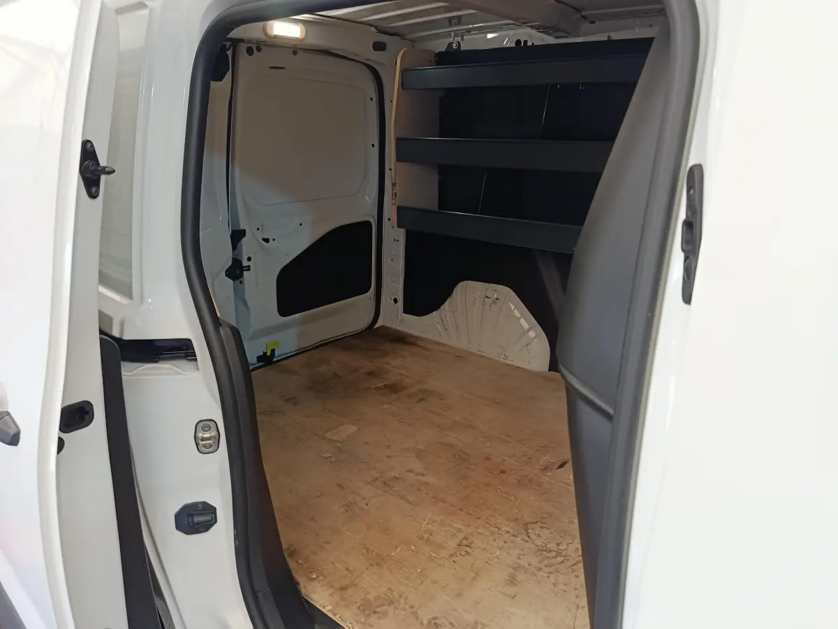Vue intérieure arrière du Citroën Berlingo blanc, montrant l’espace de chargement avec étagères noires et plancher en bois.