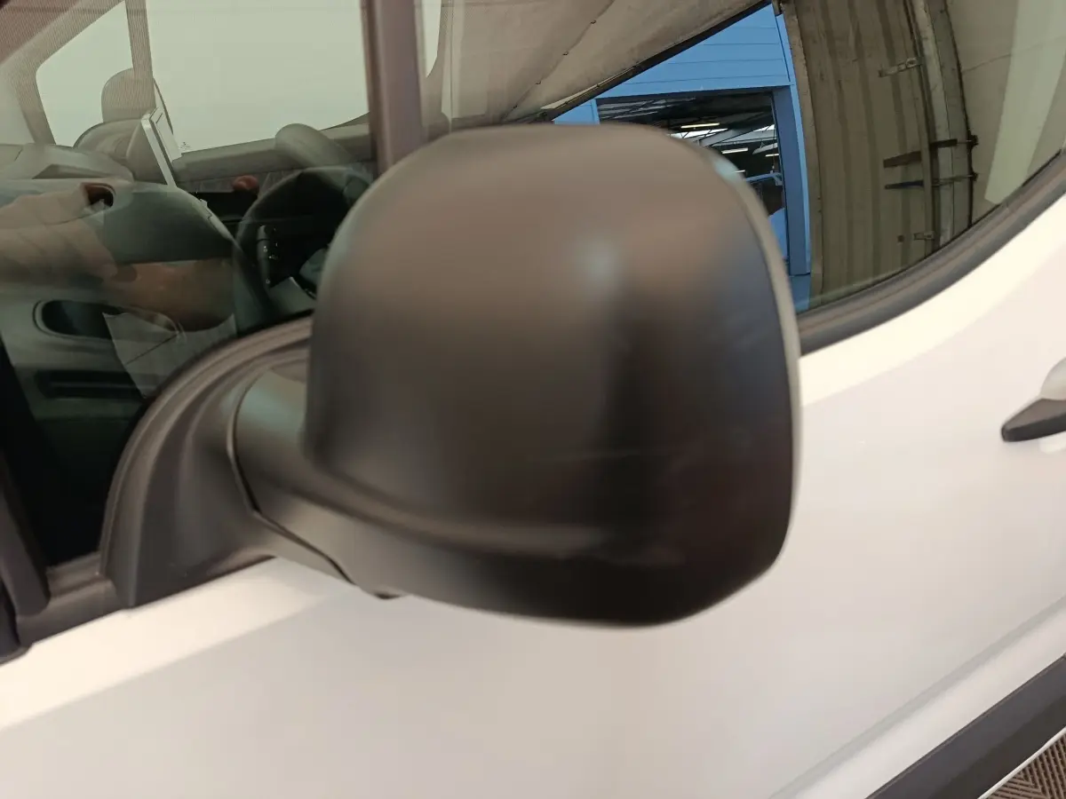 Gros plan sur le rétroviseur noir côté conducteur du Citroën Berlingo blanc, vue partielle de la porte avant.